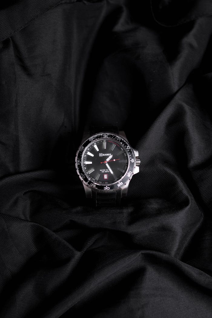 hero-img-02 Close-up of a silver wristwatch on black fabric displaying elegance and luxury.